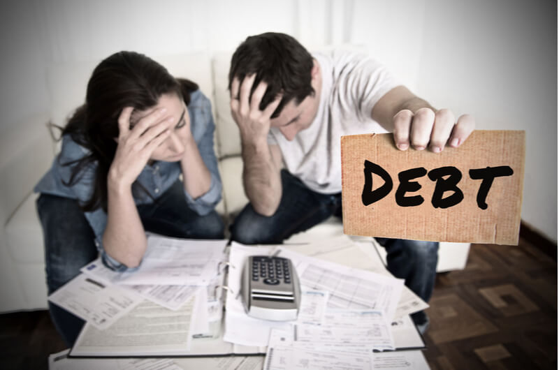 Two people looking at bills and holding a debt sign